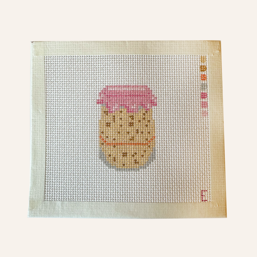 A needlepoint canvas featuring a sourdough starter pattern. The pattern showcases a jar filled with tan sourdough starter, an orange rubber band and pink lid cover. The canvas features a color palette panel and is signed by "Eloise."