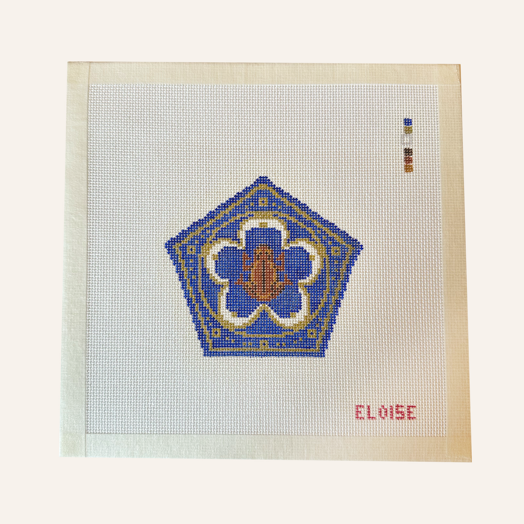 A chocolate frog needlepoint canvas designed with a blue pentagon shape with gold ornate detailing.  brown frog sits in the middle. the canvas has a color palette guide and is signed "Eloise"