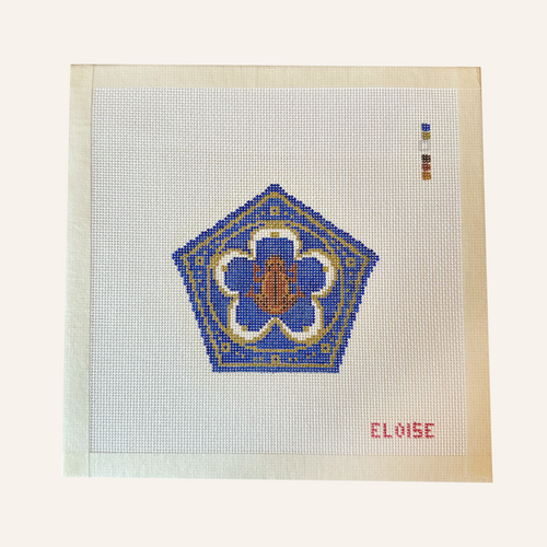 A chocolate frog needlepoint canvas designed with a blue pentagon shape with gold ornate detailing.  brown frog sits in the middle. the canvas has a color palette guide and is signed "Eloise"