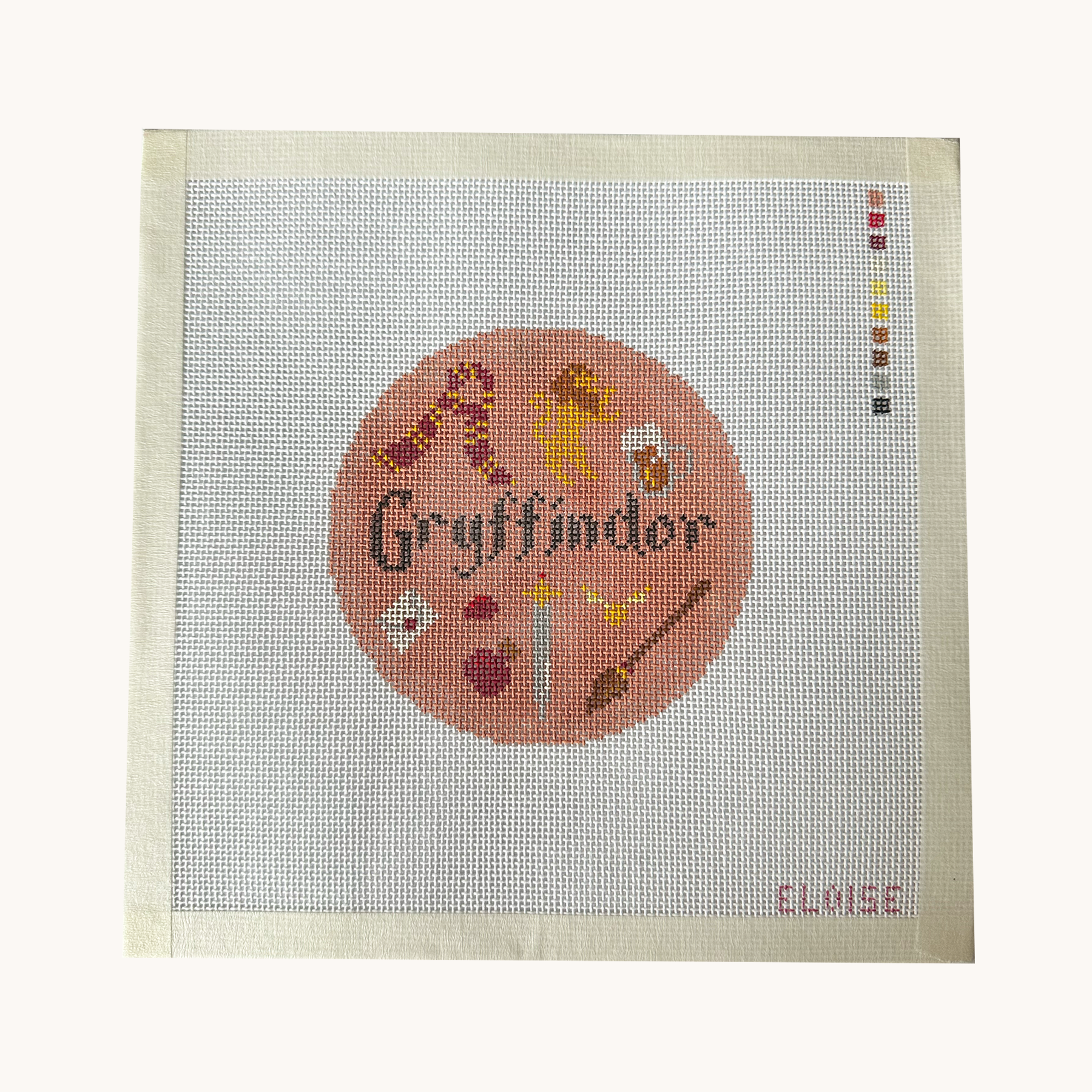 A Griffindor needlepoint canvas designed as a red circle with Griffindor motifs. the canvas has a color palette guide and is signed "Eloise"