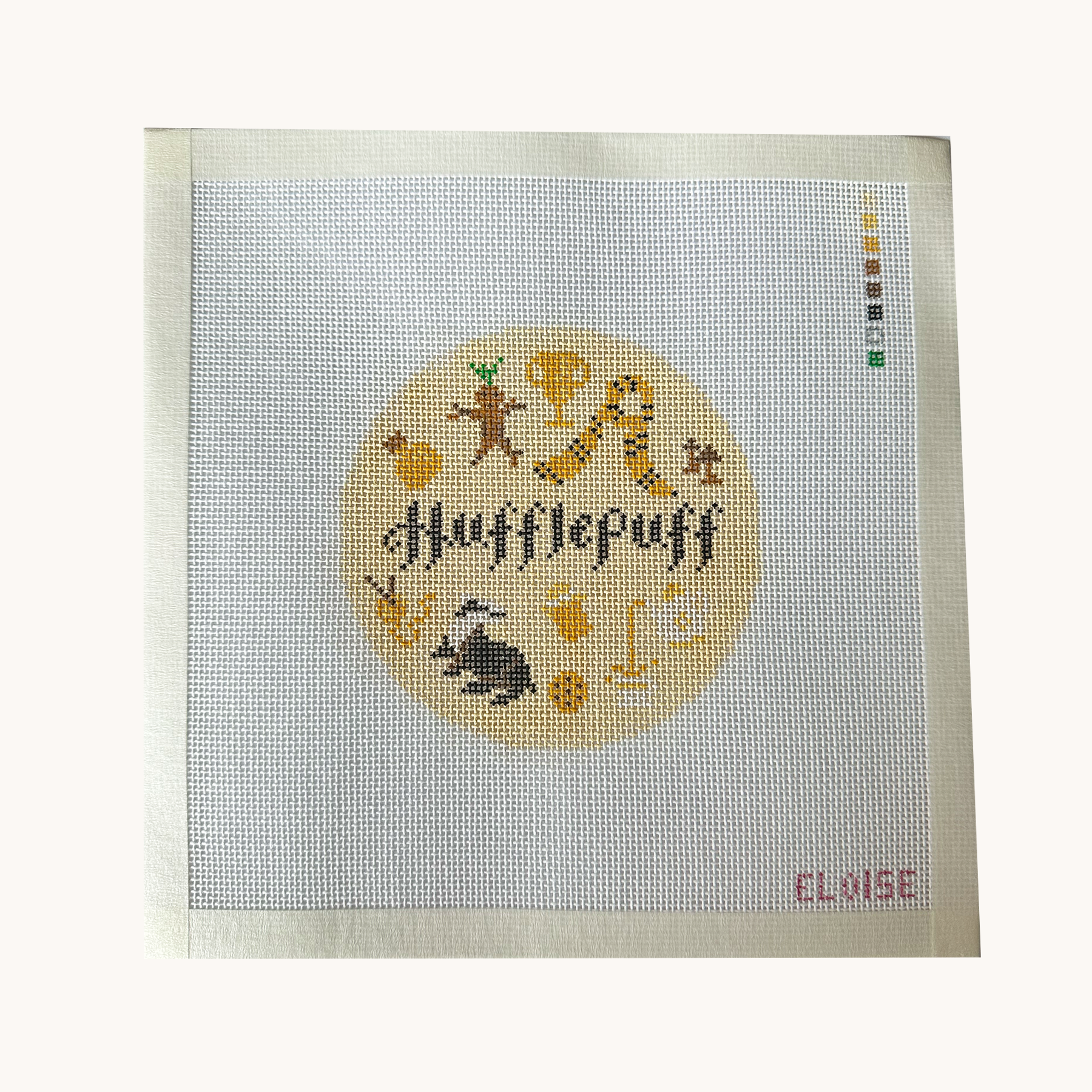 A Hufflepuff needlepoint canvas designed as a red circle with Hufflepuff motifs. the canvas has a color palette guide and is signed "Eloise"