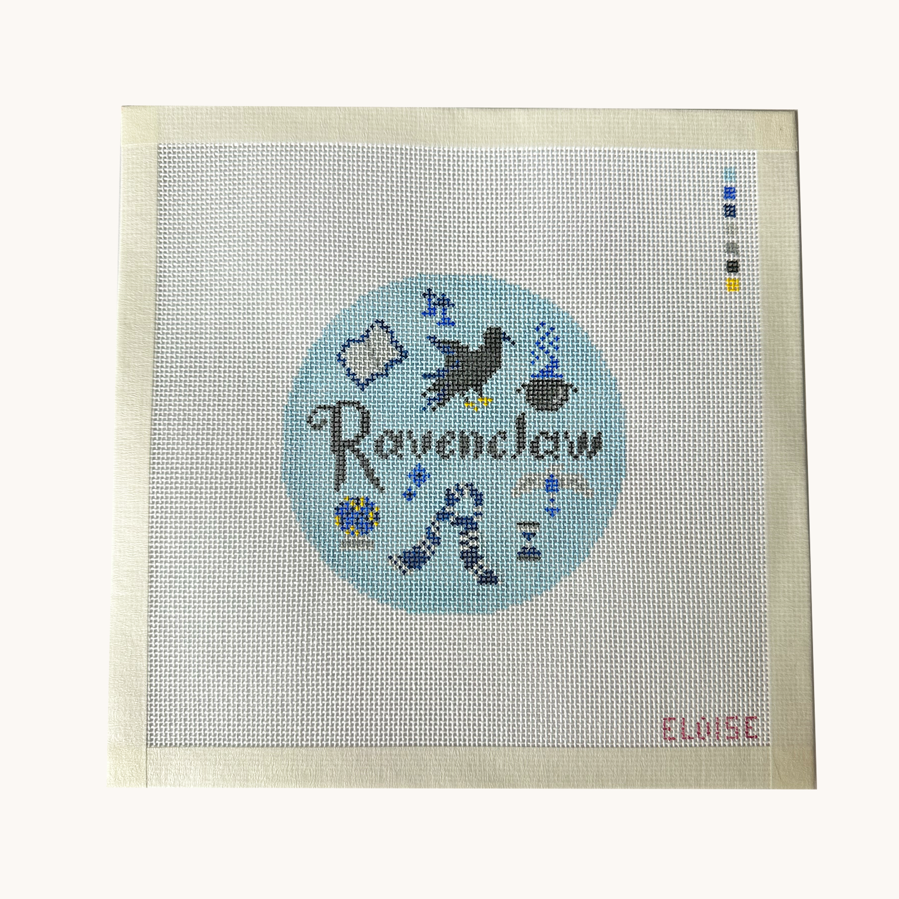 A Ravenclaw needlepoint canvas designed as a red circle with Ravenclaw motifs. the canvas has a color palette guide and is signed "Eloise"